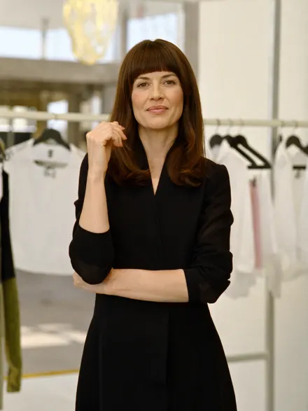 A stylist in a dark dress beside a clothes rail