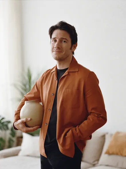 A maker in a rust jacket holding a clay pot