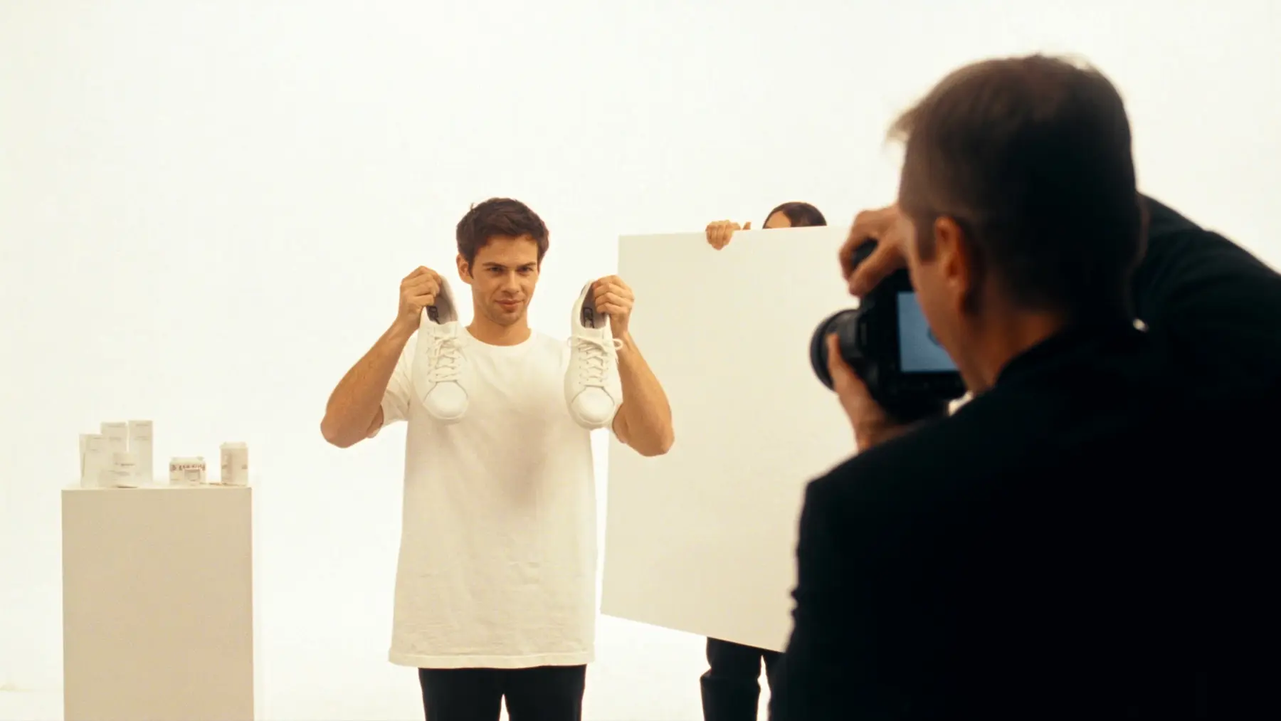 A creator holds up white trainers in a bright studio with a camera crew