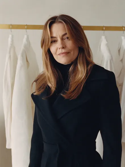 A stylist in a dark coat in front of a rail of clothes