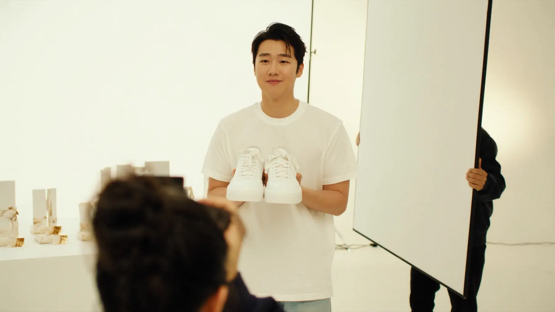 A creator holds up white trainers in a bright studio with a camera crew